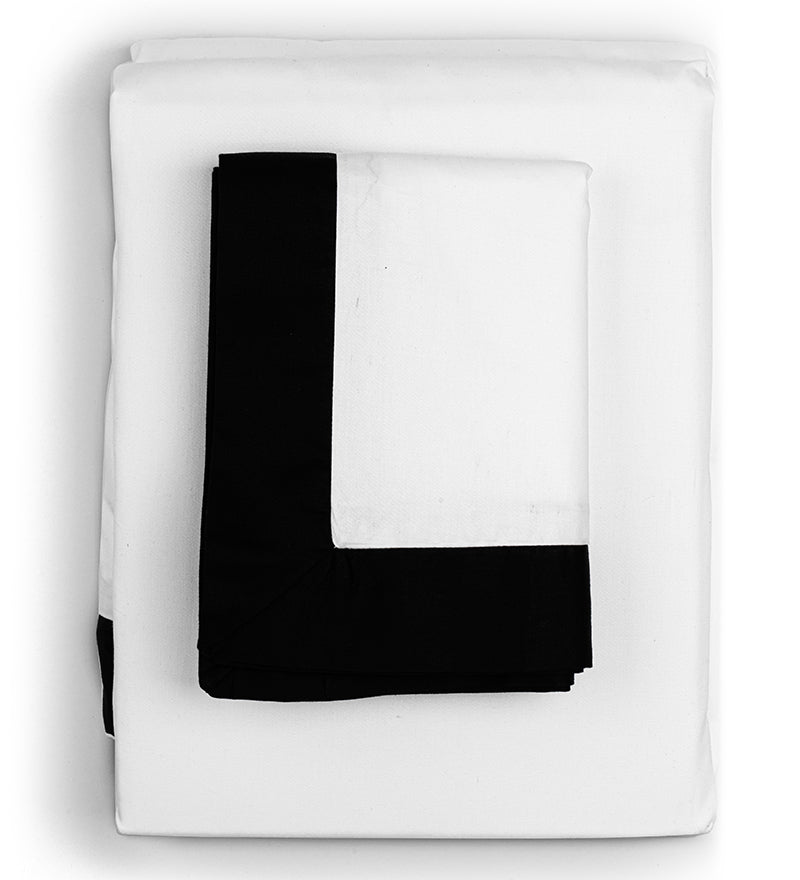 A bed with a white duvet cover and black-piped edges