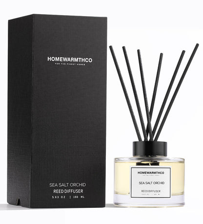 A luxury reed diffuser from HomeWarmthCo with black reeds in a clear bottle, labeled Sea Salt Orchid, with a black box packaging.