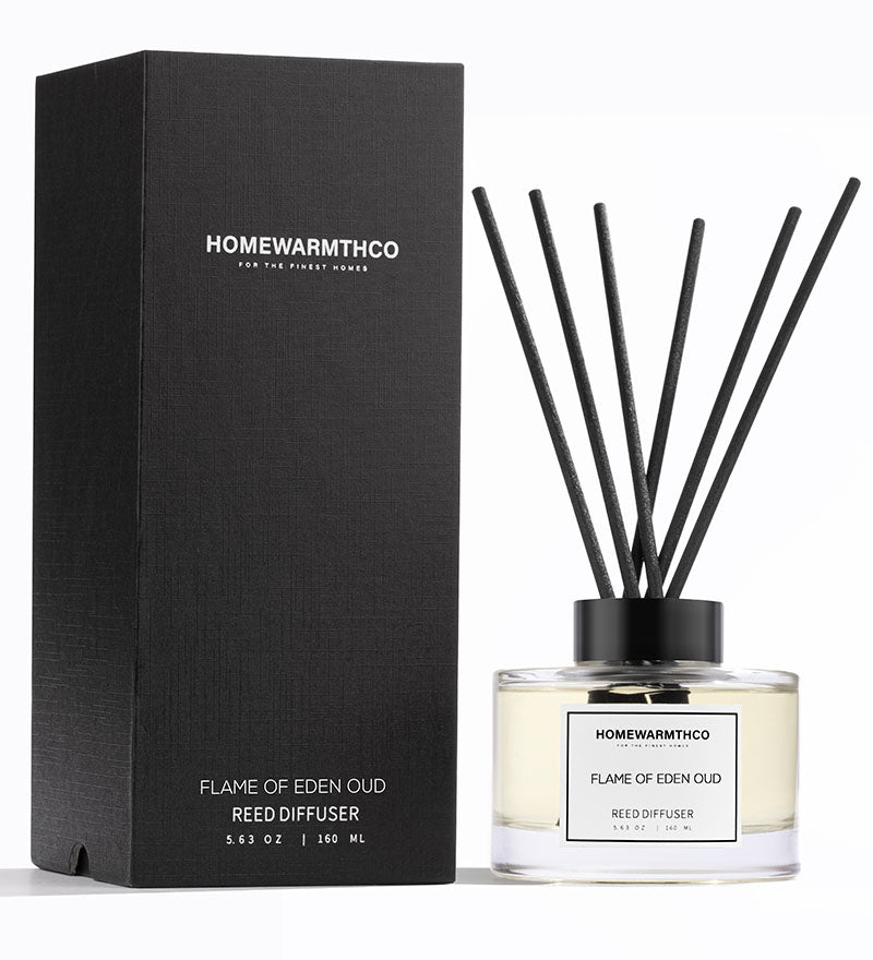 A luxury reed diffuser by HomeWarmthCo with black reeds in a clear glass bottle, featuring a black lid and label with white text. The product is displayed next to its black box packaging with the product name and brand.