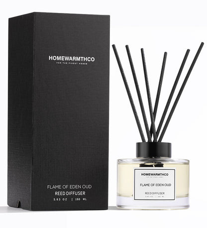 A luxury reed diffuser by HomeWarmthCo with black reeds in a clear glass bottle, featuring a black lid and label with white text. The product is displayed next to its black box packaging with the product name and brand.