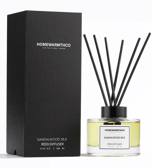 A luxury reed diffuser from HomeWarmthCo with sandalwood silk fragrance, including a black box packaging with clear glass bottle displaying the oil and black reeds.
